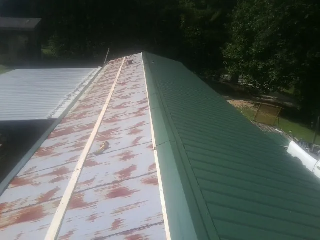 Old rusted panels beside newly installed green metal roofing — Wind Damage Roof Repair by Roofing Brothers in Bennett